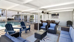 Un espacio exterior techado con mobiliario, una piscina y vistas a una casa.
