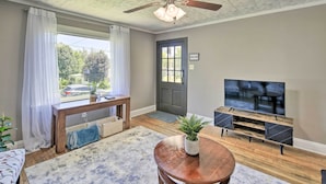 A living room with a ceiling fan, a TV on a wooden stand, a bench, and a door with a 'WELCOME' sign. - Cozy Cottage Near Dtwn Dining, Walk to Casino (Bristol)