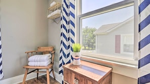 A corner room with a wooden chair, a small wooden cabinet, a window with a view of a house, and a chevron-patterned curtain. - Cozy Cottage Near Dtwn Dining, Walk to Casino (Bristol)