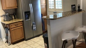 Una cucina con mobili in legno, un frigorifero in acciaio inossidabile, un piano di lavoro in granito e una finestra con persiane.