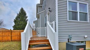A house with a wooden staircase leading to a white porch, a grey siding exterior, and an air conditioning unit on the ground. - Home away from home! Entire townhome- large backyard. Close to many colleges.  (Troy)
