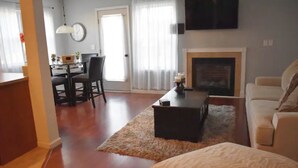 A living room with a fireplace, a sofa, a coffee table, and a dining area with chairs and a table. - Home away from home! Entire townhome- large backyard. Close to many colleges.  (Troy)