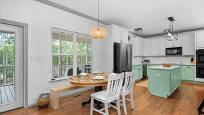 Una cocina moderna con armarios blancos, una mesa de comedor de madera y un ventanal grande.