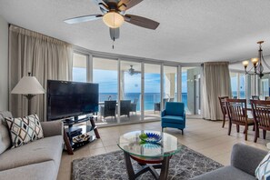 Relax in this stylish living room with a large flat-screen TV, glass coffee table, and sliding glass door leading to a balcony with ocean views.
