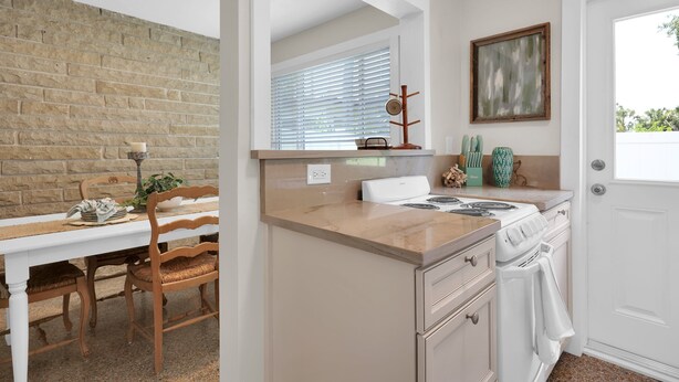 A kitchen with a white stove, a wooden dining table with chairs, a brick wall, and a window with blinds. - Here Comes The Sun! King Bed - One block to the water Unit #4 (St. Augustine)