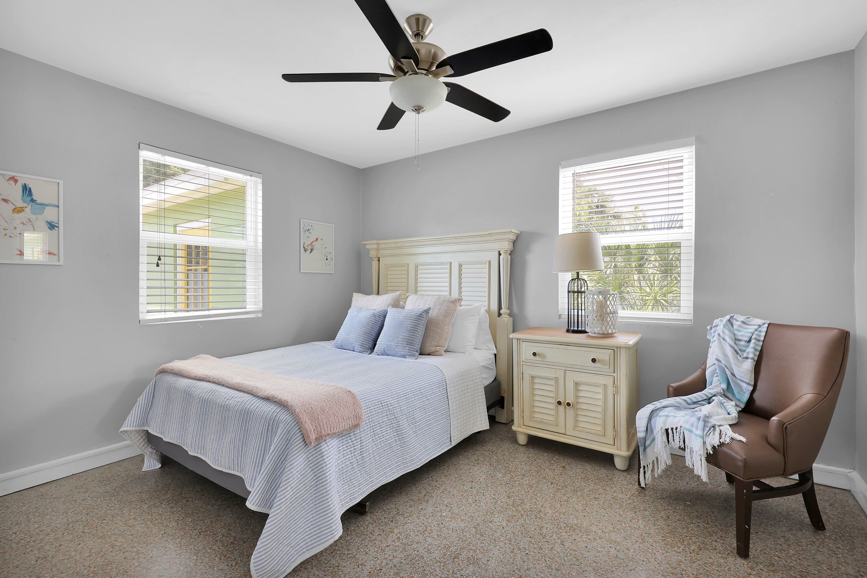 A bedroom with a bed, a chair, a nightstand, and a ceiling fan.