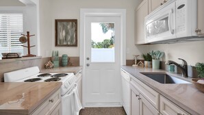 A compact kitchen with white appliances, a sink, and a door leading to a balcony. - Here Comes The Sun! King Bed - One block to the water Unit #4 (St. Augustine)