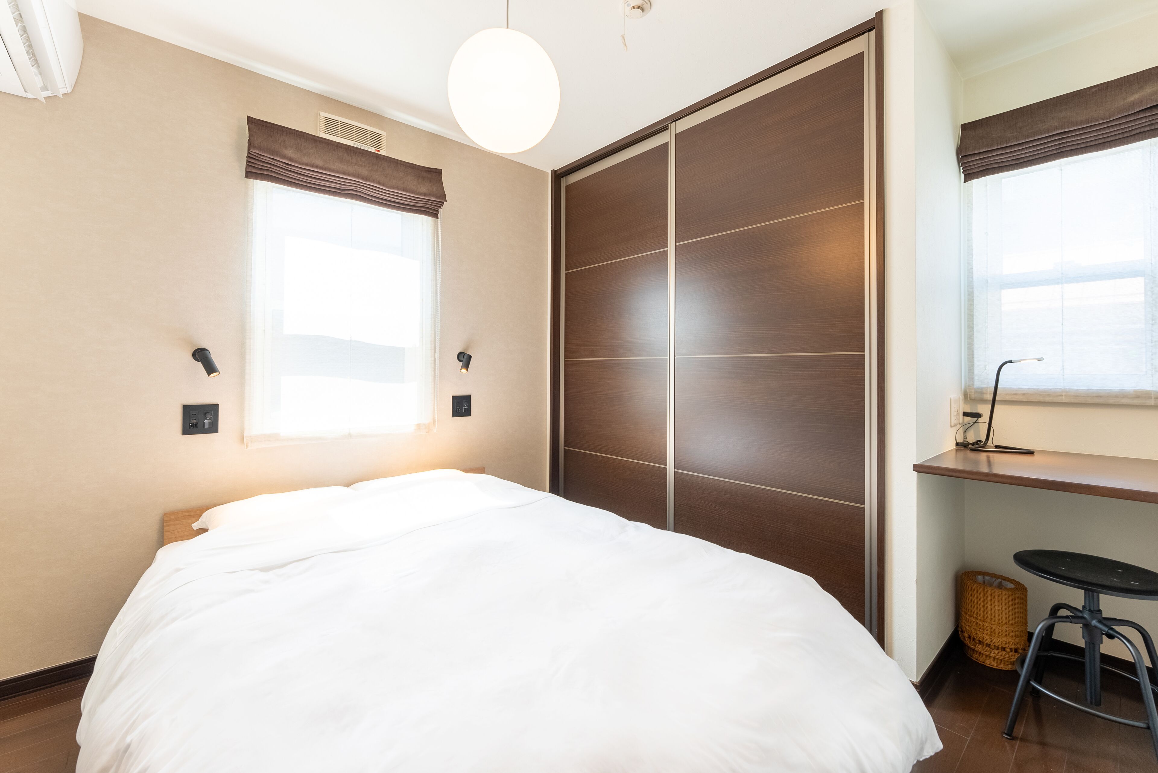 A bedroom with a bed, a wardrobe, a desk with a chair, and a window with curtains.