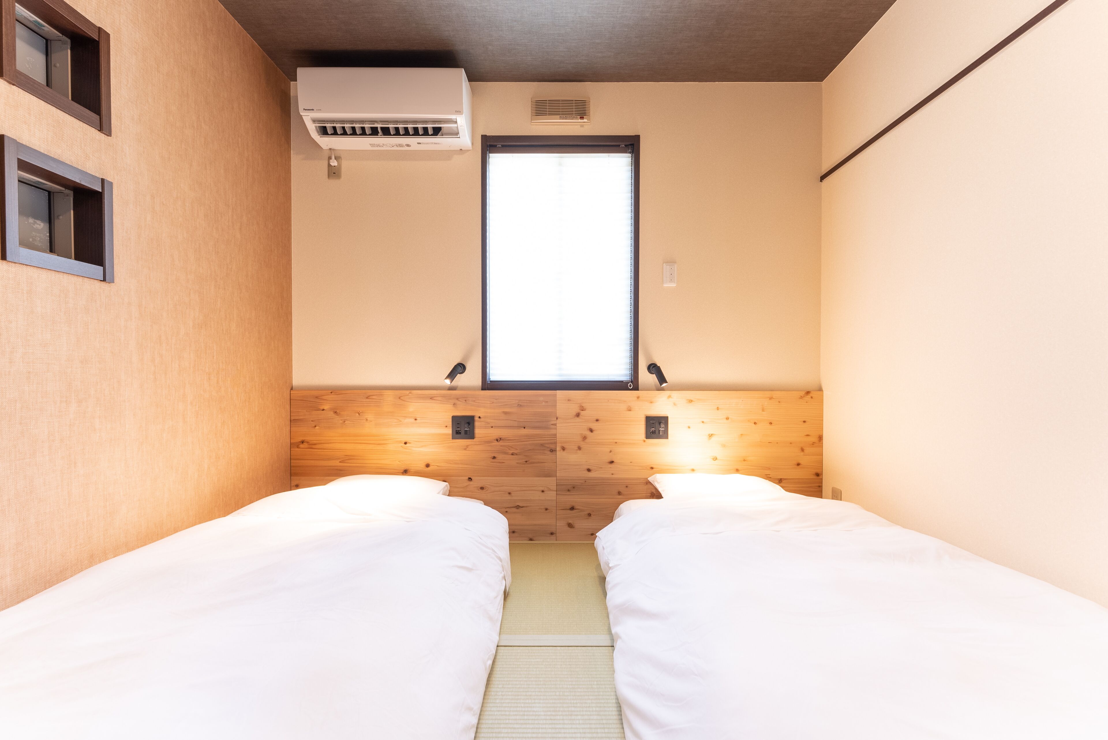 Una habitación pequeña y acogedora con dos camas individuales, una ventana y un equipo de aire acondicionado.