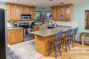 A kitchen with wooden cabinets, a central island, bar stools, and a tiled backsplash.