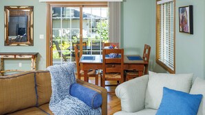 A living room with a sofa, a chair, a dining table with chairs, a large window, and a framed picture on the wall. - Downtown Fish Creek, Sleeps 6 - Yellow Birch Cottage (Fish Creek)