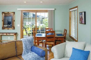 A living room with a sofa, a chair, a dining table with chairs, a large window, and a framed picture on the wall. - Downtown Fish Creek, Sleeps 6 - Yellow Birch Cottage (Fish Creek)