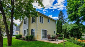 A two-story house with a patio, a lawn, and a tree. - Downtown Fish Creek, Sleeps 6 - Yellow Birch Cottage (Fish Creek)