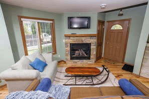 A living room with a stone fireplace, a television mounted above it, a sofa with blue cushions, and a sled on the floor. - Downtown Fish Creek, Sleeps 6 - Yellow Birch Cottage (Fish Creek)