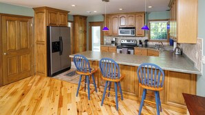 A kitchen with wooden cabinets, a stainless steel refrigerator, a microwave, and a large island with bar stools. - Downtown Fish Creek, Sleeps 6 - Yellow Birch Cottage (Fish Creek)