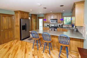 A kitchen with wooden cabinets, a stainless steel refrigerator, a microwave, and a large island with bar stools. - Downtown Fish Creek, Sleeps 6 - Yellow Birch Cottage (Fish Creek)