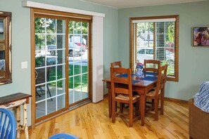 A dining area with a wooden table and chairs, a window with blinds, and a view of parked cars outside. - Downtown Fish Creek, Sleeps 6 - Yellow Birch Cottage (Fish Creek)
