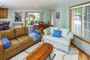 A living room with a sofa, armchair, coffee table, dining table, and kitchen area.