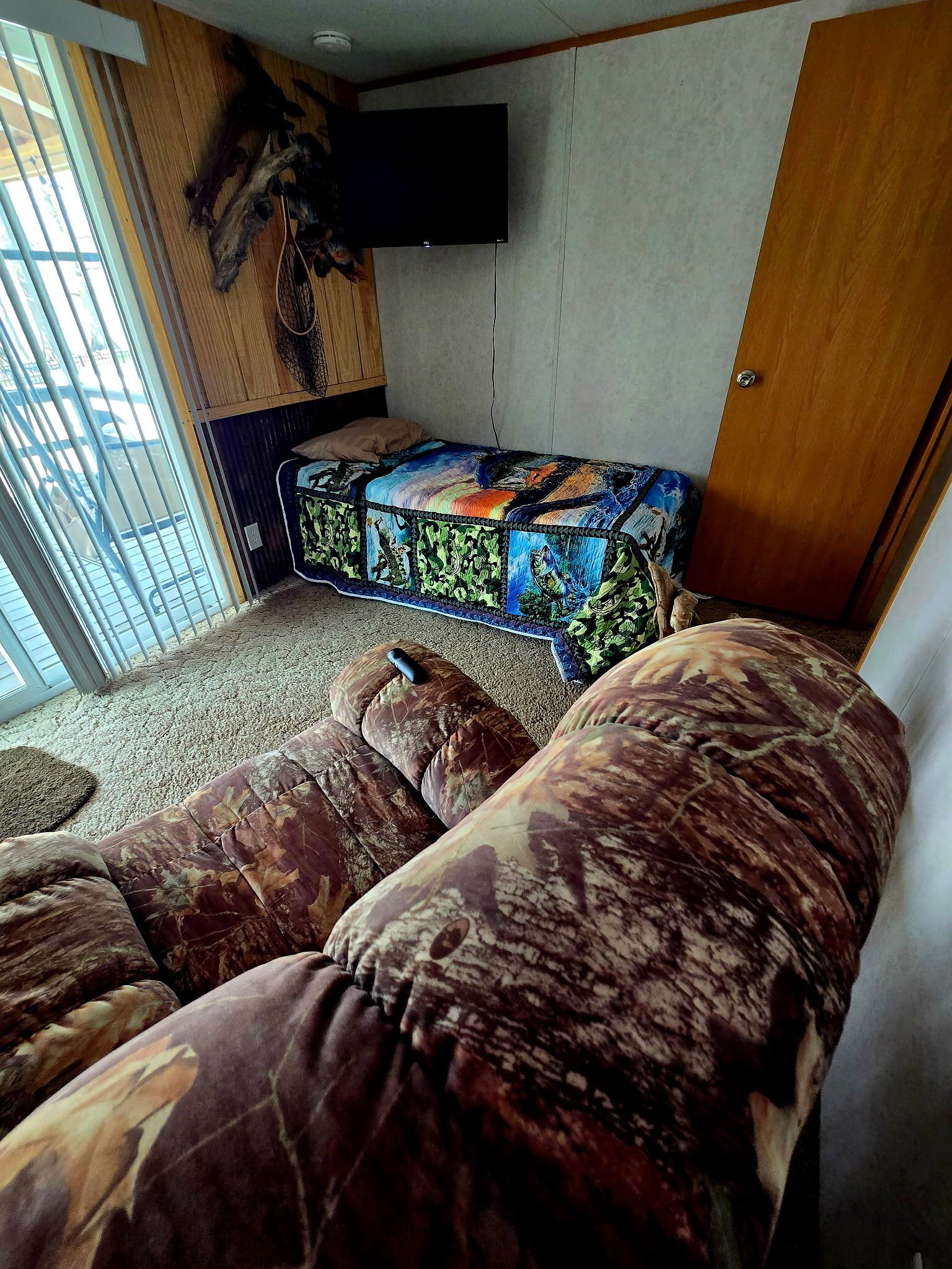 Interni accoglienti di un camper, con un divano a fantasia camouflage, un letto trapuntato dai colori vivaci e un televisore a parete.