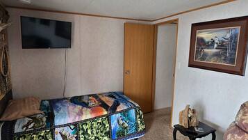 Un dormitorio con cama, televisor montado en la pared, una puerta y un cuadro enmarcado.