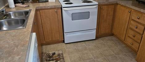 A kitchen with wooden cabinets, a white stove, a microwave, and a sink.