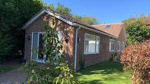 Une maison à deux étages, construite en briques, avec un toit en tuiles, un porche à l’avant et une pelouse bien entretenue.
