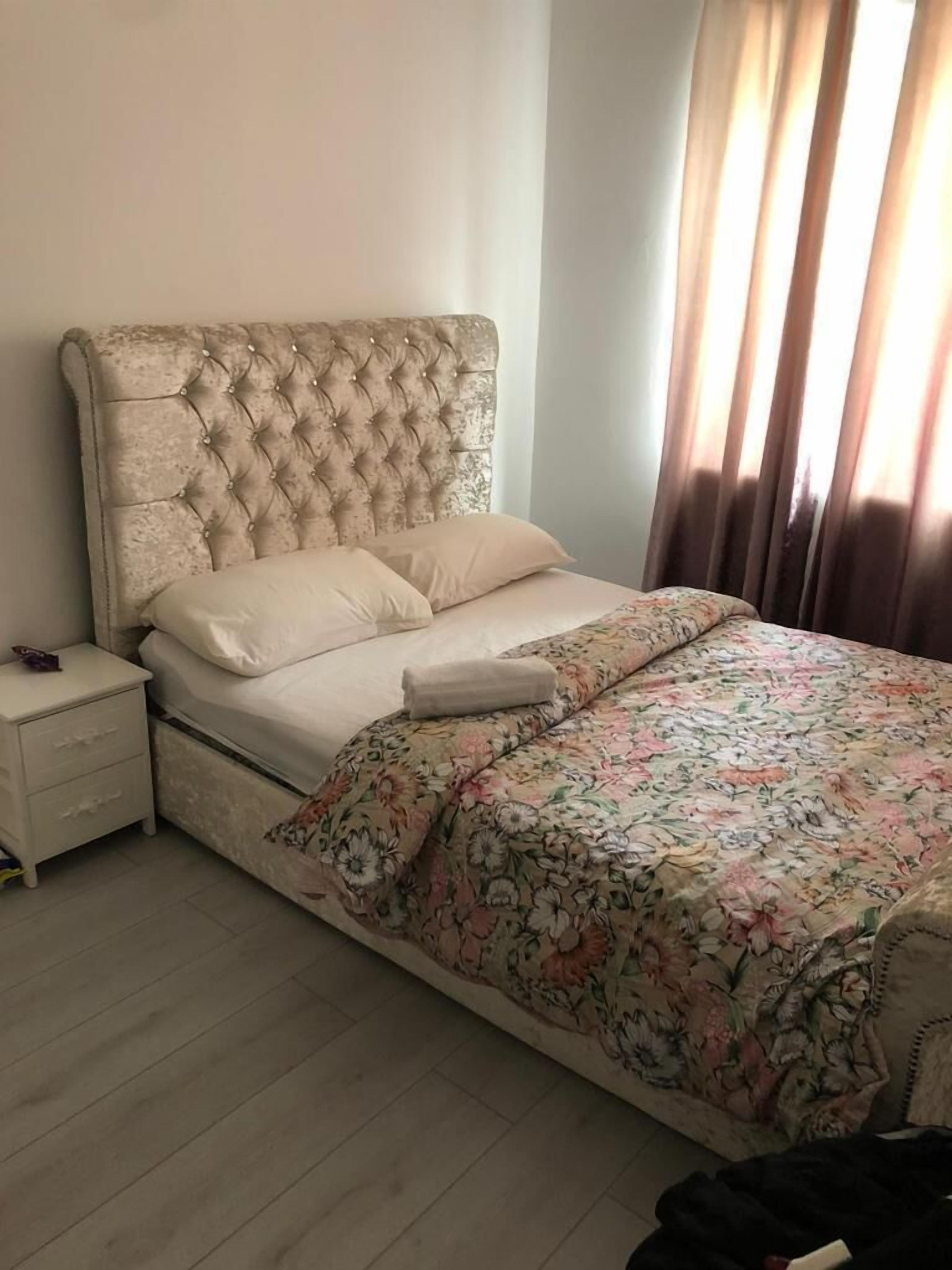 A bedroom with a tufted headboard, a floral bedspread, and a nightstand with drawers.