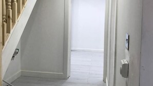 Un couloir avec un escalier en bois, des murs blancs et un sol blanc.