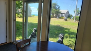 A dining area with a large table and chairs, a sliding glass door leading to a grassy yard with two stone statues, and a view of a residential neighborhood.