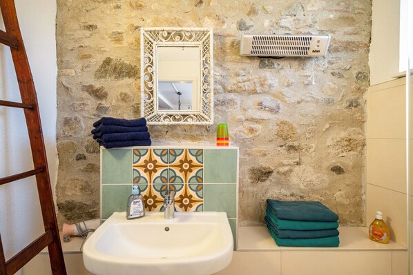 Un baño con pared de piedra, lavabo con espejo, toallero, calefactor y una botella de jabón de manos.