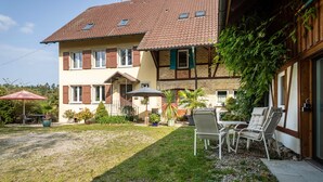 Een twee verdiepingen tellend huis met een pannendak, een veranda en een kleine tuin met buitenmeubilair.