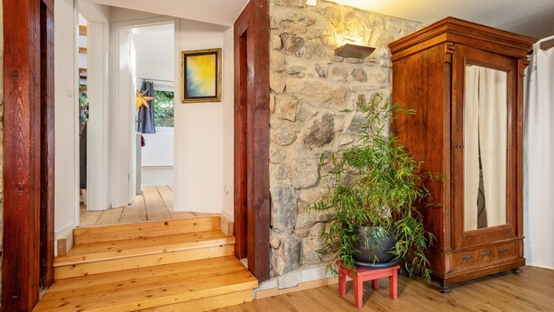 Een houten trap die leidt naar een kamer met een stenen muur, een potplant en een houten kast.