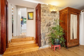 Una escalera de madera que conduce a una habitación con una pared de piedra, una planta en maceta y un armario de madera.