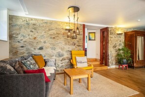A living room with a stone wall, a wooden coffee table, a sofa, a yellow armchair, and a staircase leading to another room.