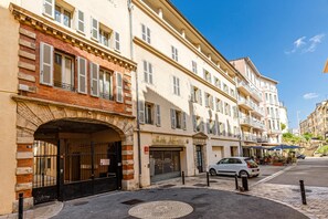 Um edifício com vários andares, entrada no nível da rua, uma placa visível e um carro estacionado.