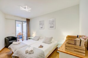 Quarto de hotel com duas camas, uma cadeira, uma mesinha de madeira e vista para o exterior.