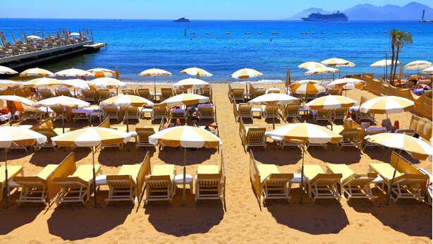 A beach with rows of sun loungers and umbrellas, a pier, and a cruise ship in the background. - Au Vieux Port Cannes City Center, Cannes, France (Cannes)
