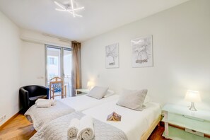 Ein Hotelzimmer mit zwei Betten, einem Sessel, einem Balkon und Bildern an den Wänden.