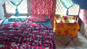 A room with a bed, a small table with a floral tablecloth, and a window with a lattice design. - Red lava show lodge (Tanna Island)