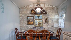 Zona pranzo con parete in pietra, sedie in legno, tavolo e diverse opere d'arte incorniciate.