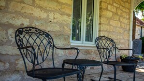 Un patio con due sedie in metallo e un tavolino, addossato a un muro in pietra con una finestra.