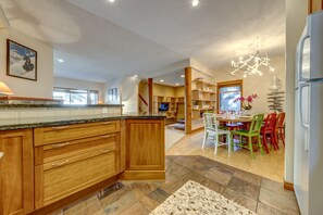 A modern kitchen with wooden cabinets, a granite countertop, and a dining area with colorful chairs. - Snowy Creek 14 - Ski in Ski out, 5 Bedrooms, Short Walk to Whistler Village (Whistler)