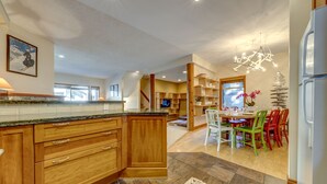 A modern kitchen with wooden cabinets, a granite countertop, and a dining area with colorful chairs. - Snowy Creek 14 - True Ski in Ski out, easy walk to Whistler Village, Private Garage. (Whistler)