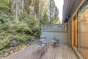 Eine Holzterrasse mit zwei Metallstühlen, umgeben von einem Holzzaun und dichtem Grün.