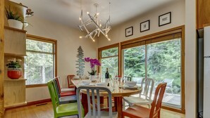 A dining area with a wooden table, colorful chairs, and large windows offering a view of the outdoors. - Snowy Creek 14 - True Ski in Ski out, easy walk to Whistler Village, Private Garage. (Whistler)