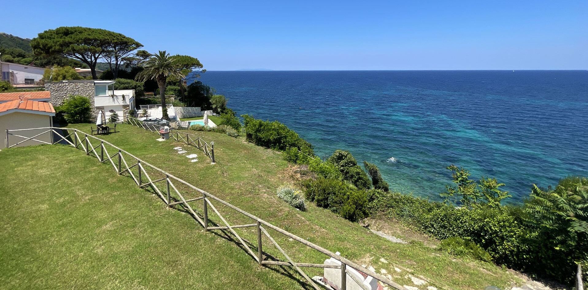 A coastal property with a grassy lawn, a wooden fence, and a view of the sea.