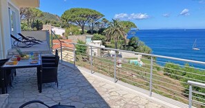 Une terrasse avec une table dressée pour le dîner, offrant une vue dégagée sur la côte, la mer et les bateaux.