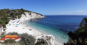A coastal beach with clear waters, a rocky shoreline, and a few boats.