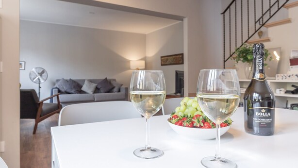 Ein Esstisch mit zwei Weingläsern und einer Flasche Bolla Wein, einer Schale Trauben und einer Schale Erdbeeren.