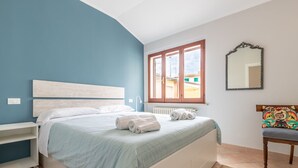 Ein Schlafzimmer mit einem Bett, einem Nachttisch, einem Stuhl, einem Fenster und einem Spiegel.